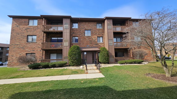Front view of a four-story brick apartment building with balconies.