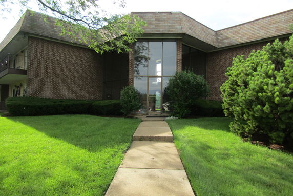 Front view of a brick building with a large glass entrance and sloped roof.