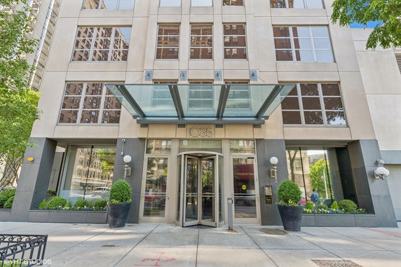 Front view of a multi-story building entrance with a glass canopy and revolving door.
