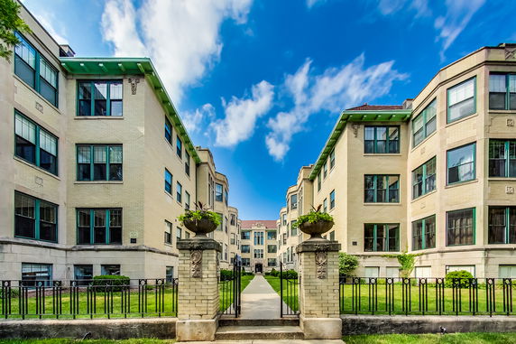 Front view of a multi-story residential building with multiple windows and entrance pathway.