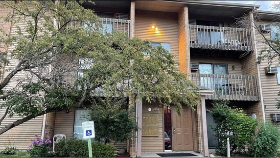 Front view of a multi-story building with balconies and a tree in front.