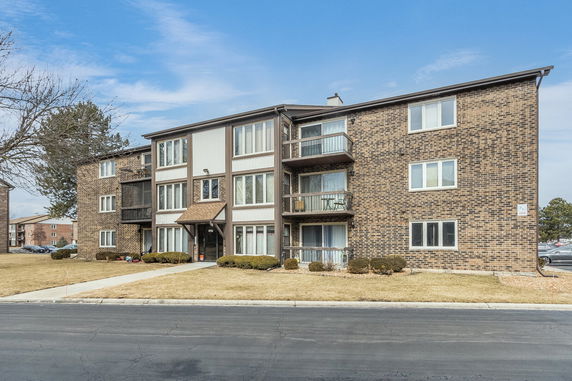 Front view of a three-story brick apartment building with balconies.