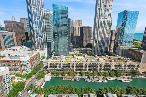 Panoramic view of tall city buildings with a river and boats in the foreground.
