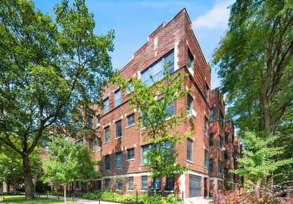 Front view of a brick apartment building with multiple windows and trees around.