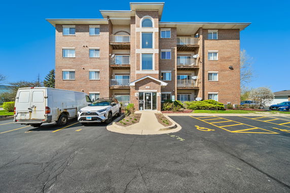 Front view of a four-story brick apartment building with balconies and a central entrance.
