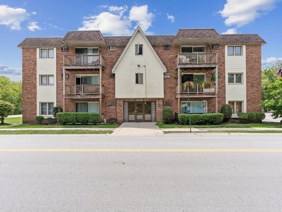 Front view of a three-story apartment building with brick and beige siding and balconies.