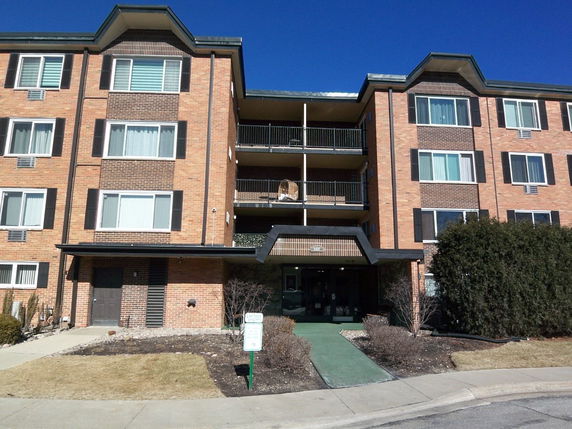 Front view of a multi-story brick residential building with balconies and large windows.