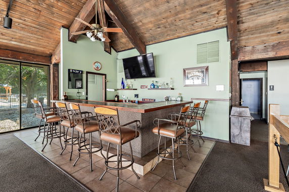 Interior view of a clubhouse bar area with a wooden ceiling, modern bar counter, and barstools.