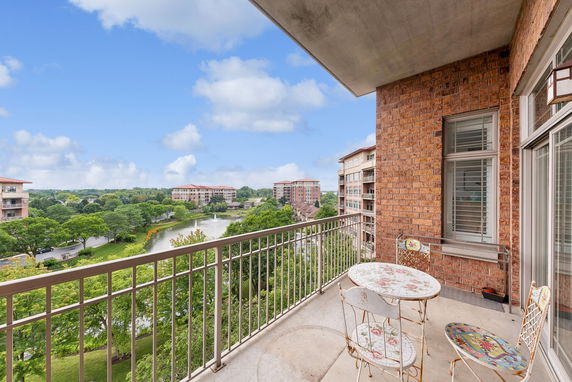 Balcony with metal railing and patio furniture, overlooking a scenic view of buildings and greenery.
