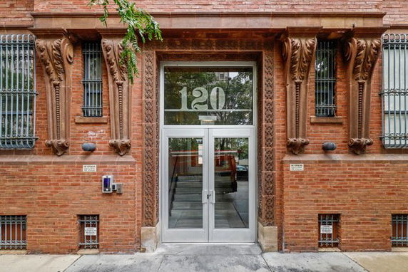 Front view of a building entrance with decorative brickwork and metal bars on windows.