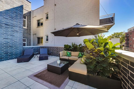 Rooftop area with lounge seating, an umbrella, and ambient plants.