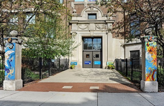 Front view of a building entrance with decorative pillars and a metal fence.