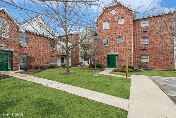 Front view of a multi-story brick apartment building with green doors.