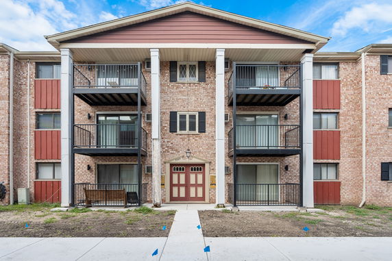 Front view of a three-story building with balconies and brick exterior.