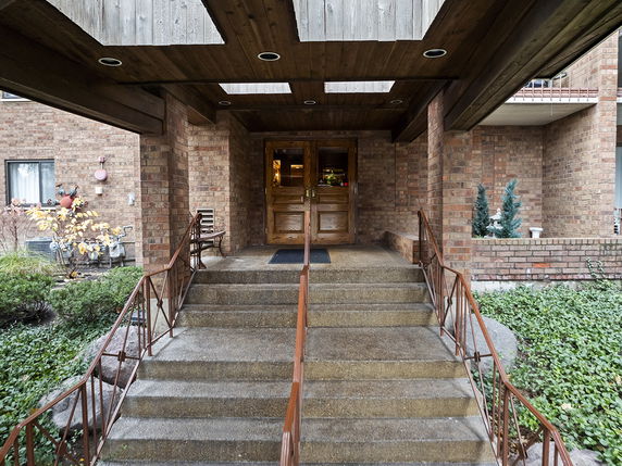 Front view of a building entrance with brick walls and a set of stairs leading to double wooden doors.