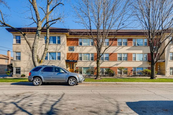 Front view of a multi-story apartment building with trees and parked car.