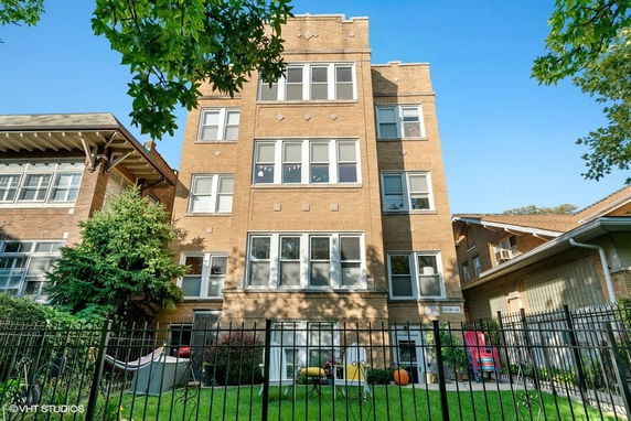 Front view of a multi-story brick building with several windows and a fenced yard.