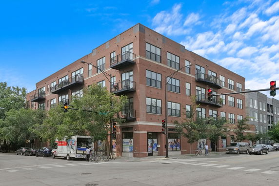 Front view of a multi-story brick building with balconies on a street corner.