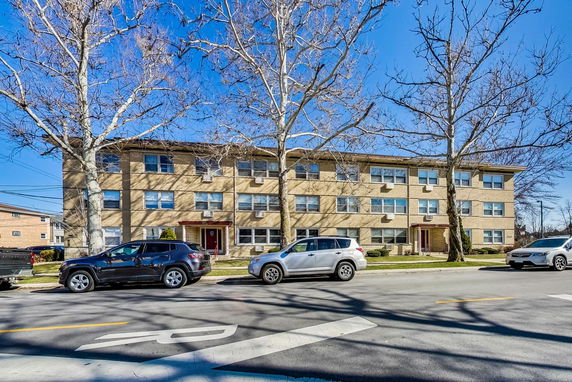 Front view of a three-story brick apartment building with windows and trees in front.