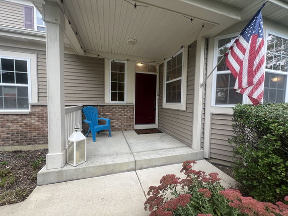 Front view of a house with a covered porch, American flag, and blue chair.