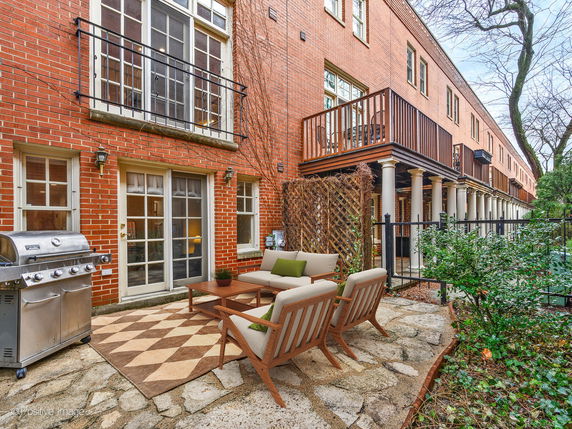 Front view of a multi-story brick house with balconies and patio furniture.