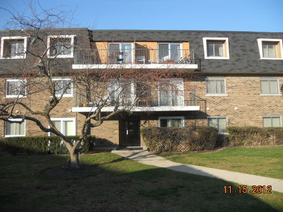 Front view of a multi-story brick building with balconies and a sloped roof.