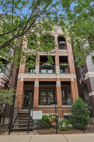 Front view of a multi-story brick building with balconies and a gated entrance.