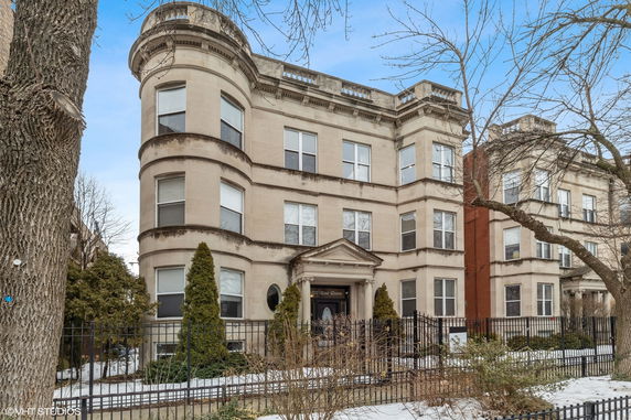 Front view of a classical three-story building with ornate architectural details and a gated entrance.