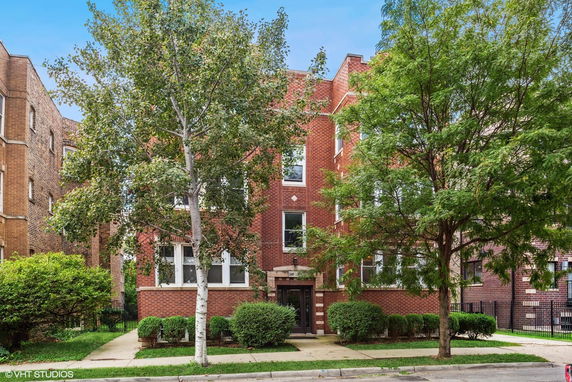 Front view of a multi-story brick building with trees and shrubs.
