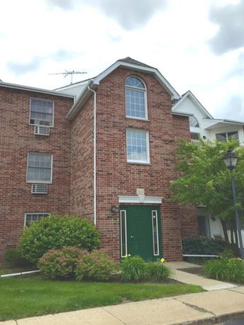 Front view of a three-story brick building with a green door and large windows.