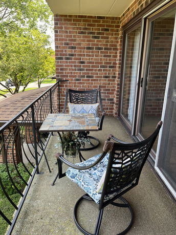 Balcony with two chairs and a table overlooking surrounding greenery.