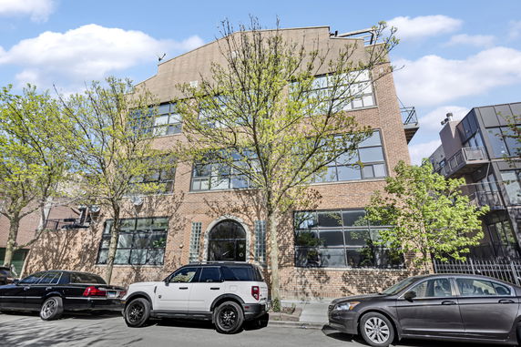 Front view of a large brick building with multiple windows and parked cars in front.