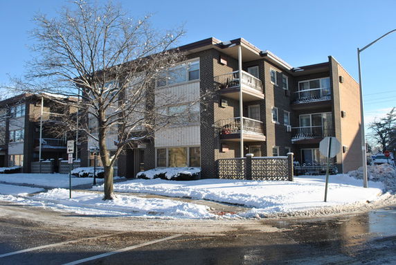 Front view of a three-story apartment building with balconies, in a snowy setting.
