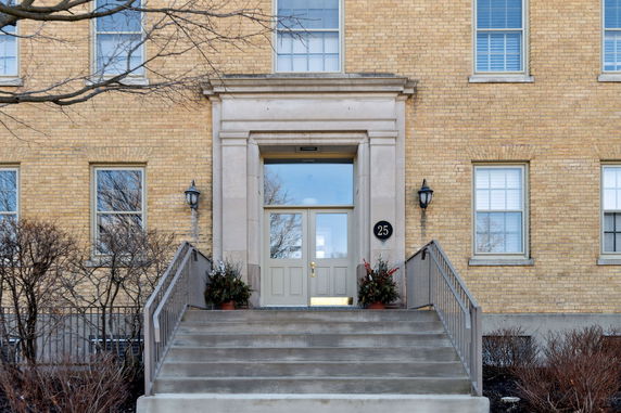 Front view of a building entrance with stairs leading up to double doors and windows on a brick facade.
