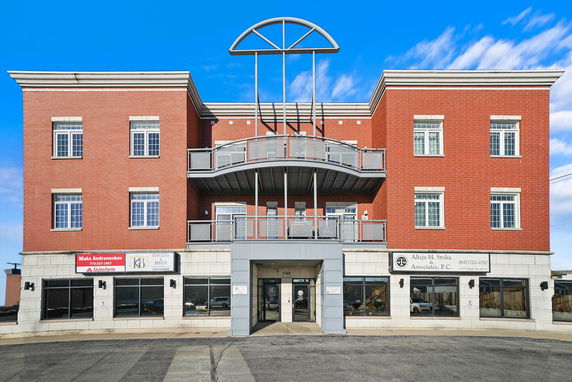 Front view of a three-story commercial building with red brick facade and large windows.