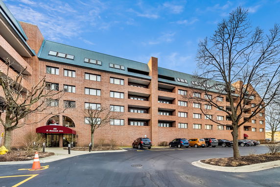 Front view of a multi-story brick apartment building with parking area.