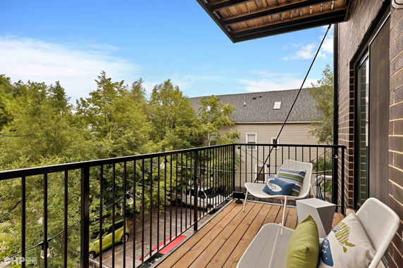 Outdoor balcony with seating overlooking trees and neighboring house.