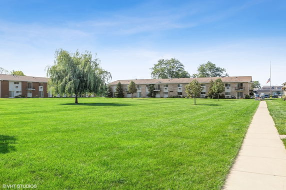 Front view of an apartment building with a large grassy area in the foreground.