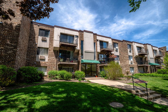 Front view of a multi-story brick apartment building with balconies and green awnings.