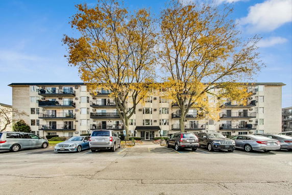 Front view of a multi-story apartment building with balconies and parked cars in front.