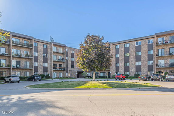 Front view of a multi-story apartment building with balconies and parking area.
