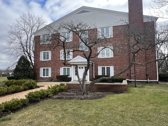 Front view of a multi-story brick building with white framed windows and a gabled roof.