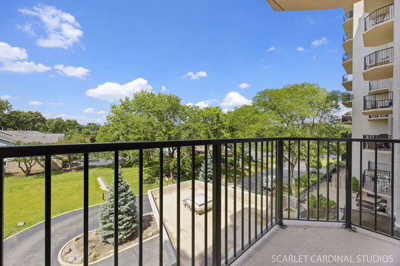 View from a balcony showing a landscaped area with trees and adjacent buildings.