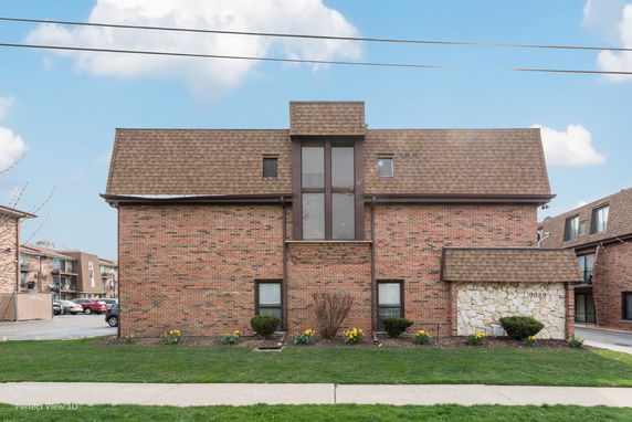 Front view of a brick building with a distinctive brown shingle roof and central vertical window feature.