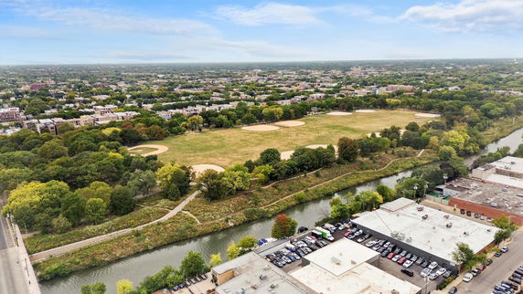 Aerial panoramic view of a park with multiple baseball fields surrounded by a river and urban area.