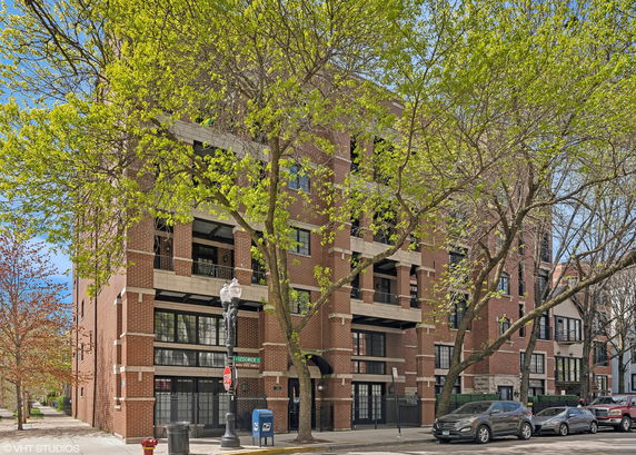 Front view of a multi-story brick apartment building on a street corner with trees.