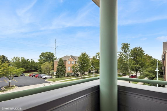 View from a balcony overlooking a residential area with trees and parking lot.