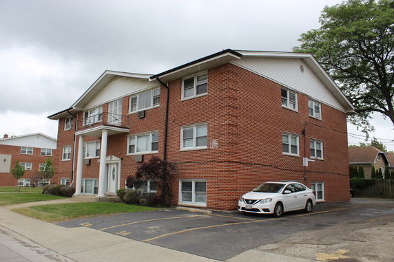 Front view of a two-story brick apartment building with multiple windows and a white car parked outside.