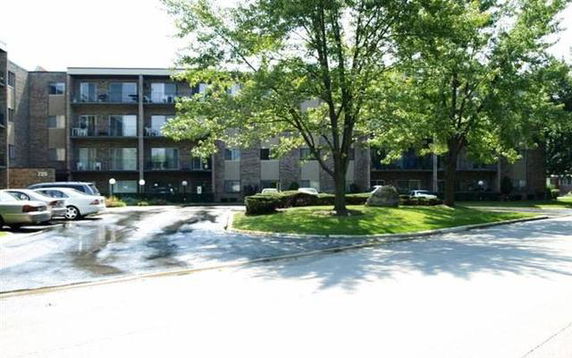 Front view of a multi-story residential building with balconies and a parking area in front.