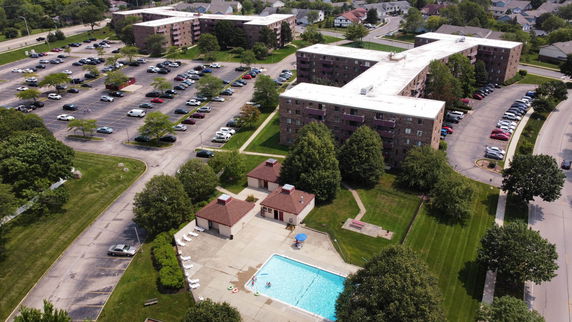 Aerial view of a residential complex with multiple buildings, parking areas, and a swimming pool.